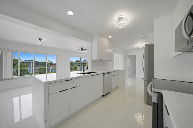 kitchen featuring kitchen peninsula, tasteful backsplash, white cabinets, sink, and appliances with stainless steel finishes