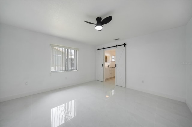 unfurnished bedroom featuring a barn door, ceiling fan, connected bathroom, and light tile floors