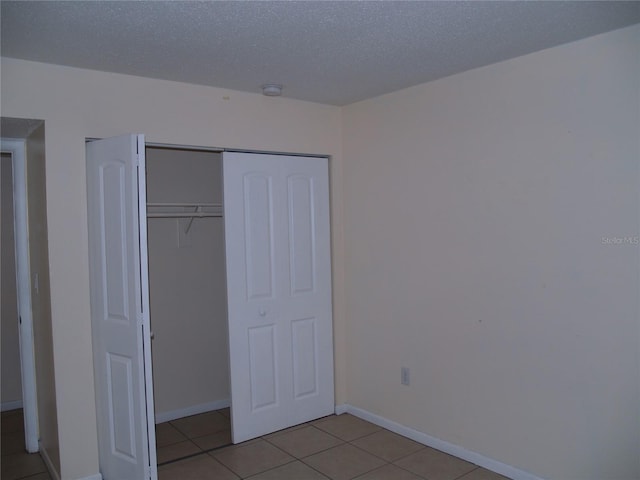 unfurnished bedroom featuring a textured ceiling, a closet, and light tile floors