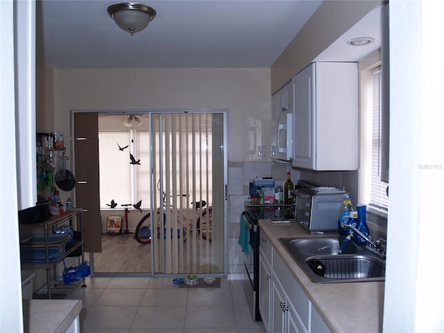 kitchen with electric range, sink, white cabinetry, and light tile floors