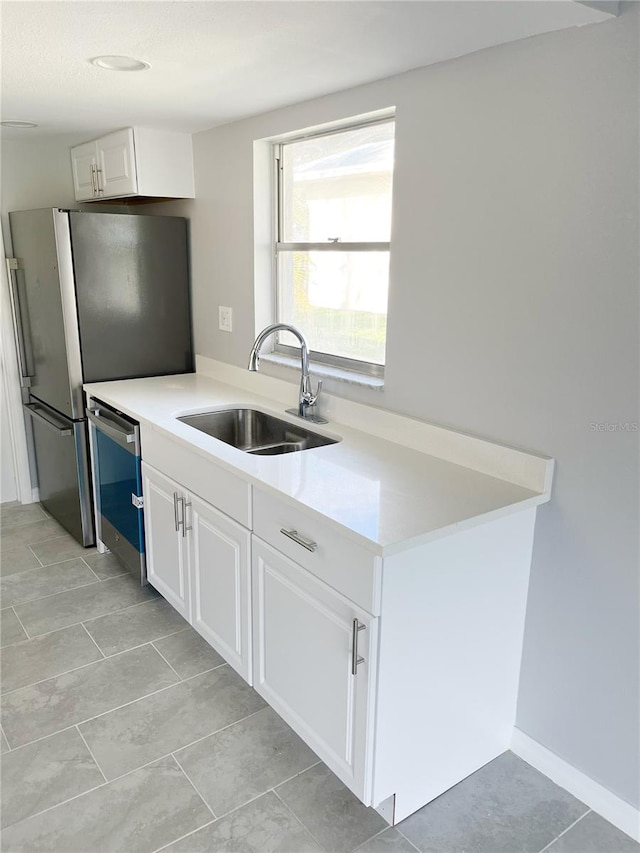 kitchen featuring white cabinetry, sink, light tile flooring, and stainless steel dishwasher