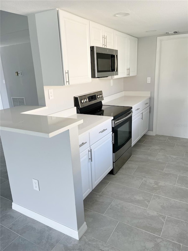 kitchen featuring light tile flooring, kitchen peninsula, white cabinets, and appliances with stainless steel finishes