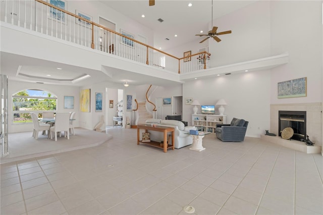 tiled living room with ceiling fan, a tray ceiling, a tile fireplace, and a towering ceiling