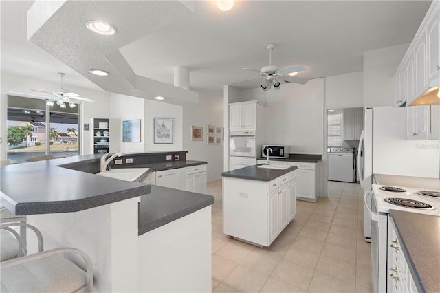 kitchen with white cabinets, white appliances, a kitchen island with sink, and sink