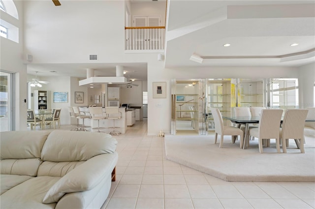 tiled living room with ceiling fan, a towering ceiling, a wealth of natural light, and a tray ceiling