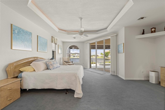 bedroom with dark carpet, ceiling fan, a raised ceiling, a textured ceiling, and access to exterior