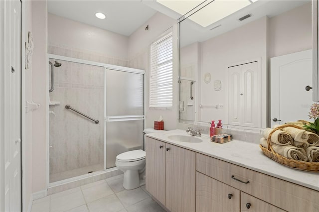 bathroom with tile patterned flooring, toilet, a shower with shower door, a skylight, and vanity