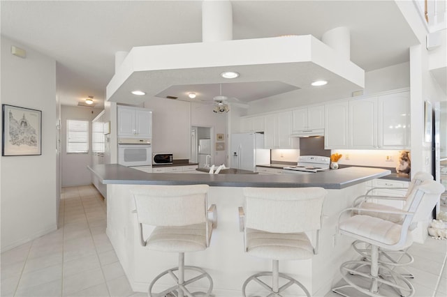 kitchen featuring a large island, white cabinets, light tile patterned floors, white appliances, and a breakfast bar