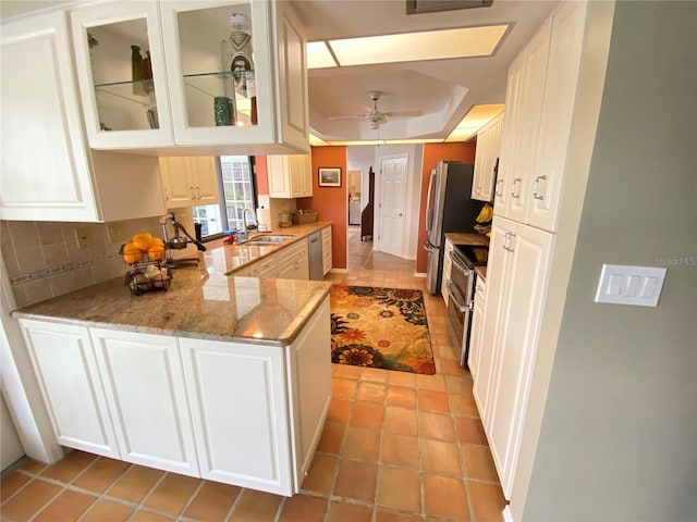 kitchen with a tray ceiling, kitchen peninsula, sink, tasteful backsplash, and ceiling fan