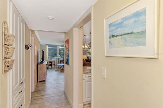 corridor featuring ornamental molding, a notable chandelier, and light wood-type flooring