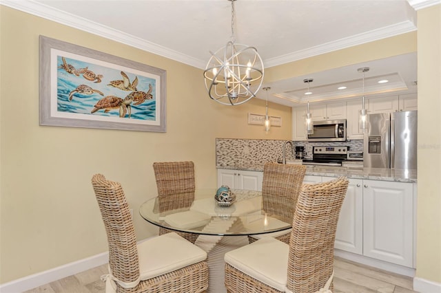 dining space with crown molding, a raised ceiling, a chandelier, and light wood-type flooring