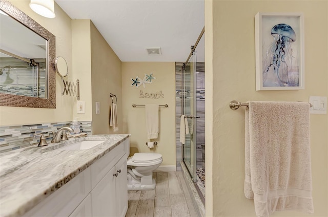 bathroom with toilet, vanity, wood-type flooring, decorative backsplash, and a shower with shower door