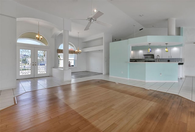 unfurnished living room with french doors, ceiling fan with notable chandelier, high vaulted ceiling, sink, and light tile floors