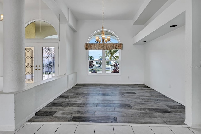 unfurnished dining area featuring an inviting chandelier, dark tile flooring, and french doors