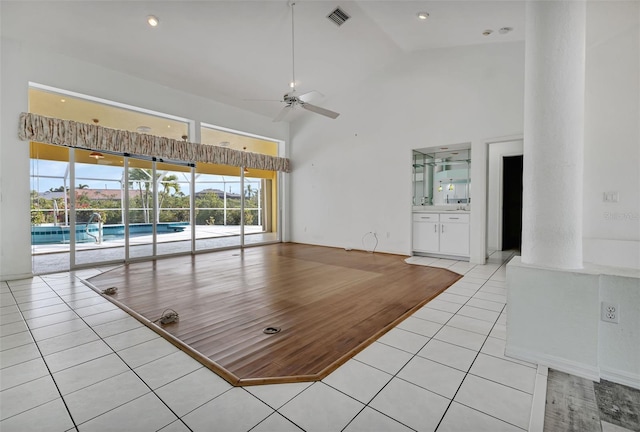 unfurnished living room with high vaulted ceiling, ceiling fan, and light tile floors