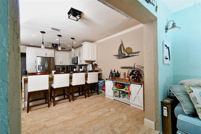 kitchen with stainless steel appliances, white cabinetry, ornamental molding, light tile floors, and pendant lighting