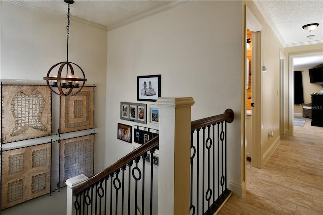 corridor featuring a notable chandelier, ornamental molding, light hardwood / wood-style floors, and a textured ceiling