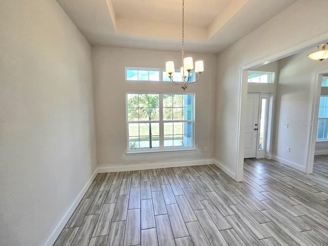 unfurnished room featuring light hardwood / wood-style flooring, a raised ceiling, and an inviting chandelier