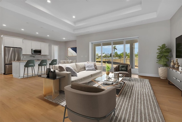 living room with light hardwood / wood-style floors and a tray ceiling