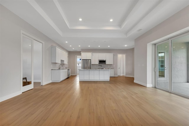 kitchen featuring a raised ceiling, white cabinets, light wood-type flooring, and stainless steel appliances