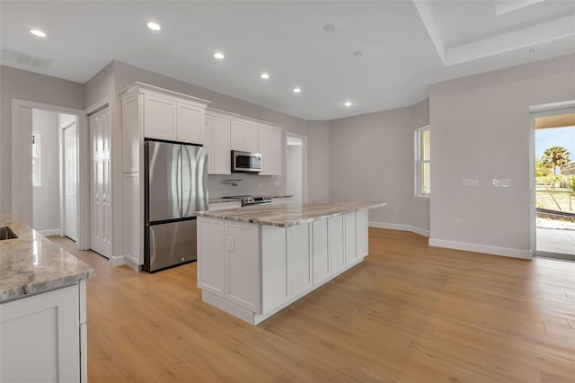 kitchen featuring light hardwood / wood-style flooring, appliances with stainless steel finishes, white cabinetry, light stone counters, and a kitchen island