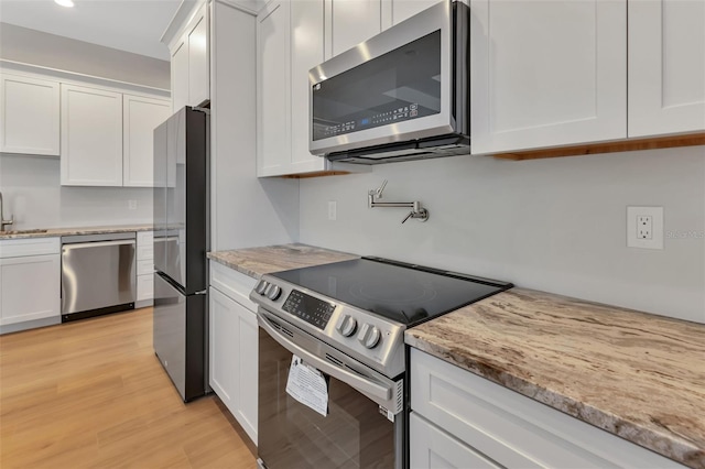 kitchen with light stone countertops, appliances with stainless steel finishes, white cabinets, light wood-type flooring, and sink