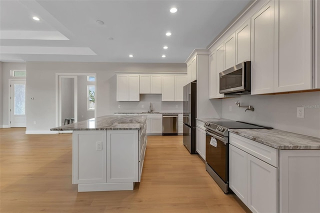 kitchen with light hardwood / wood-style floors, white cabinets, a kitchen island, stainless steel appliances, and light stone counters