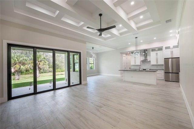 unfurnished living room with beam ceiling, coffered ceiling, ceiling fan, and light hardwood / wood-style flooring