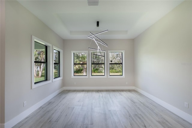 spare room with a tray ceiling and light hardwood / wood-style floors