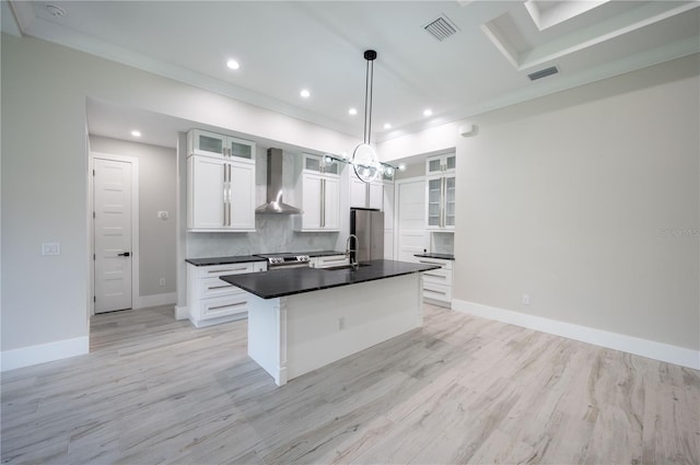 kitchen with light hardwood / wood-style flooring, hanging light fixtures, white cabinetry, an island with sink, and wall chimney exhaust hood