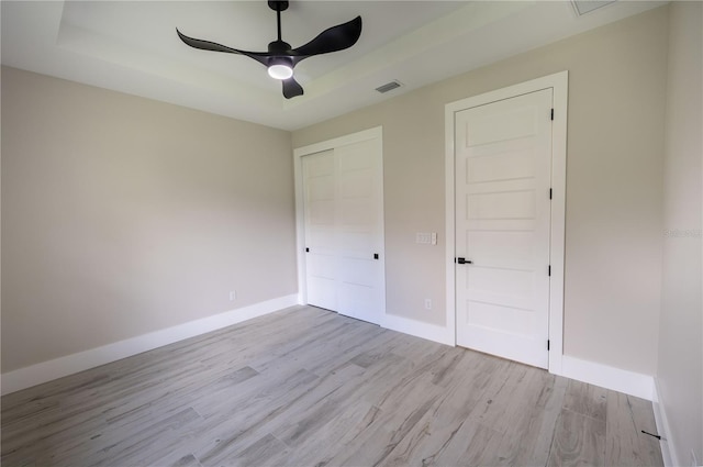 unfurnished bedroom with ceiling fan, light hardwood / wood-style floors, and a raised ceiling