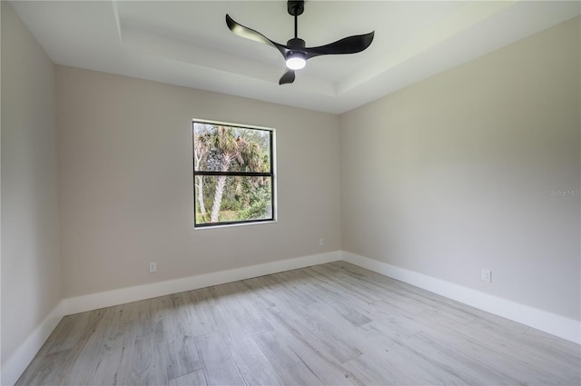 spare room featuring a tray ceiling, ceiling fan, and light hardwood / wood-style flooring