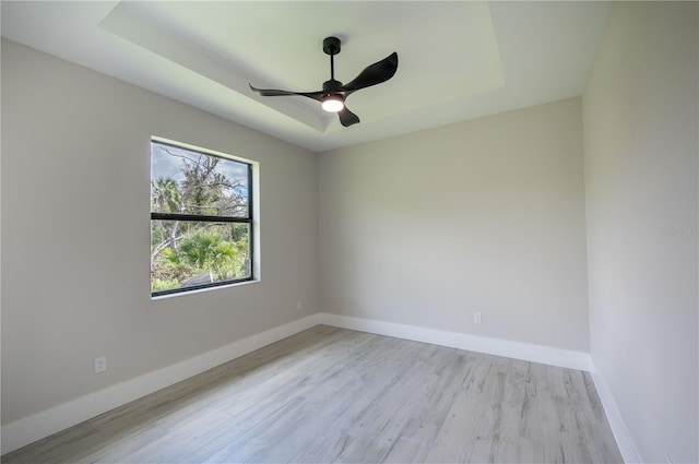 unfurnished room with a raised ceiling, ceiling fan, and light wood-type flooring