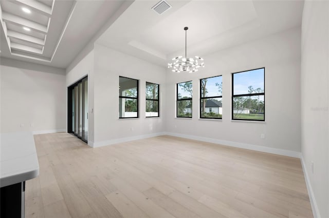 unfurnished room featuring a raised ceiling, a chandelier, and light hardwood / wood-style floors