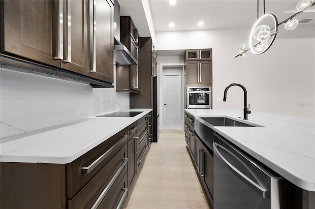 kitchen with sink, decorative light fixtures, black appliances, light stone countertops, and wall chimney range hood