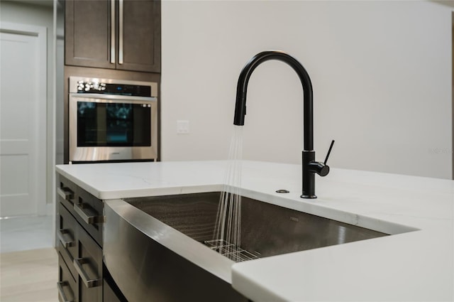 details with sink, dark brown cabinets, light stone countertops, and stainless steel oven