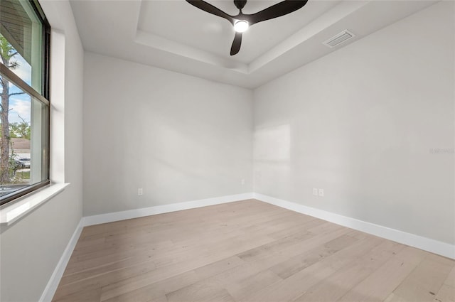 unfurnished room featuring a raised ceiling, ceiling fan, and light wood-type flooring