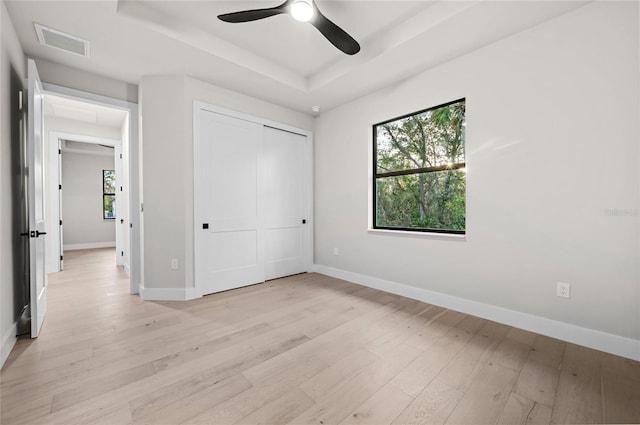 unfurnished bedroom featuring ceiling fan, a tray ceiling, a closet, and light wood-type flooring