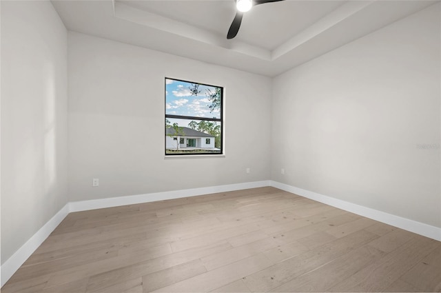 unfurnished room featuring ceiling fan, a tray ceiling, and light wood-type flooring