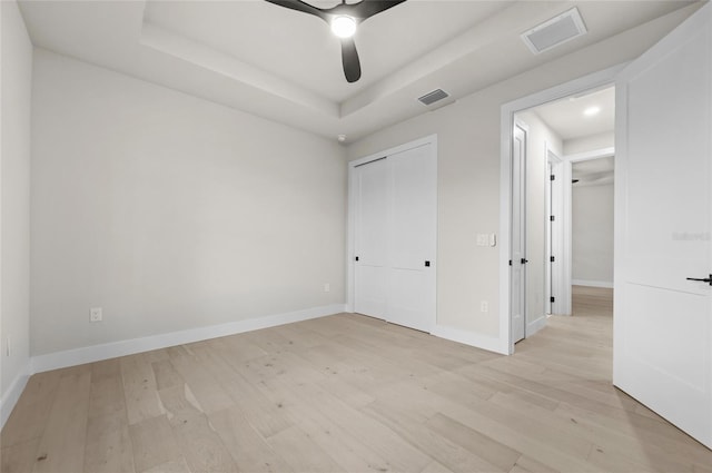 unfurnished bedroom featuring ceiling fan, a raised ceiling, a closet, and light hardwood / wood-style flooring