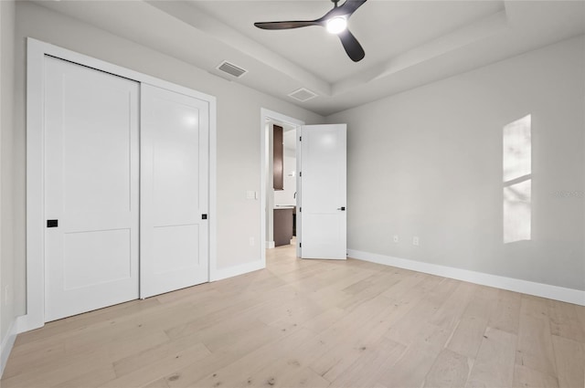 unfurnished bedroom with a closet, light hardwood / wood-style flooring, a raised ceiling, and ceiling fan