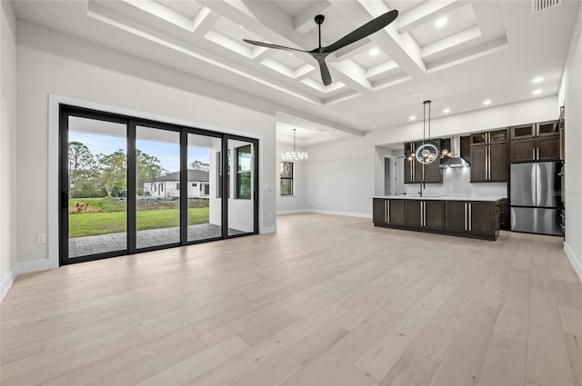 unfurnished living room with sink, a towering ceiling, coffered ceiling, ceiling fan with notable chandelier, and light wood-type flooring