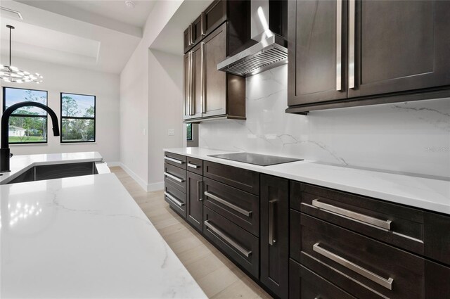 kitchen featuring decorative light fixtures, sink, backsplash, light stone countertops, and wall chimney exhaust hood