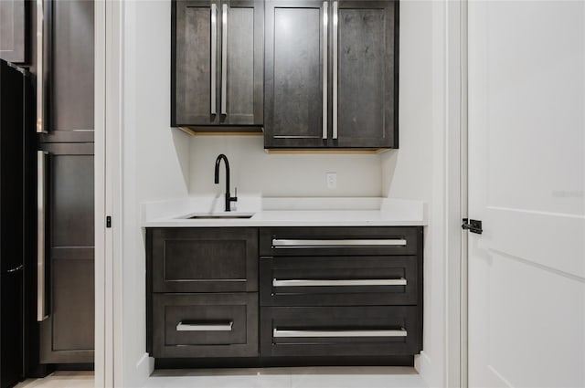 bar featuring paneled refrigerator, sink, and dark brown cabinets