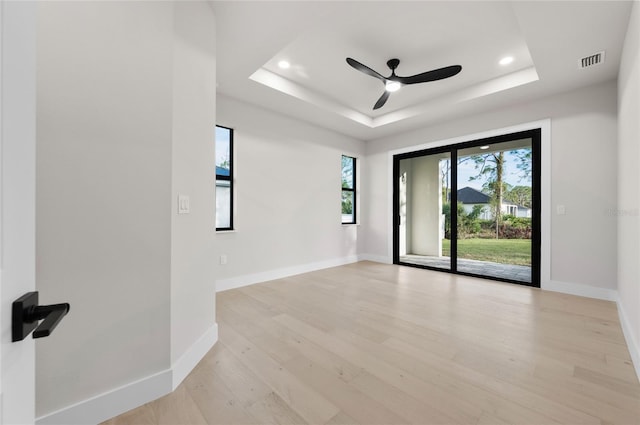 empty room with ceiling fan, light wood-type flooring, and a tray ceiling