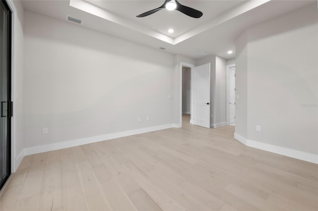 spare room featuring a raised ceiling, ceiling fan, and light hardwood / wood-style flooring