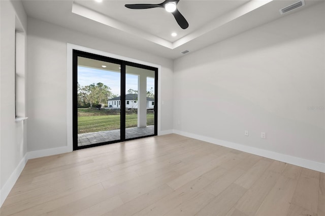 spare room with a tray ceiling, light hardwood / wood-style floors, and ceiling fan