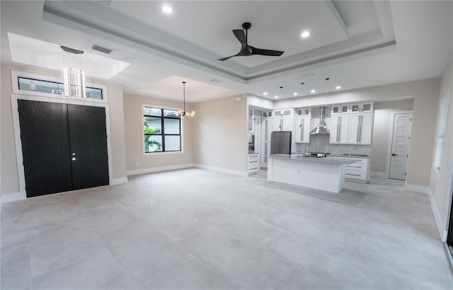 kitchen featuring white cabinets, a kitchen island, decorative light fixtures, a raised ceiling, and wall chimney exhaust hood