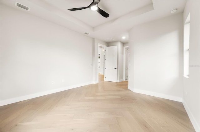 unfurnished room with ceiling fan, light parquet flooring, and a raised ceiling