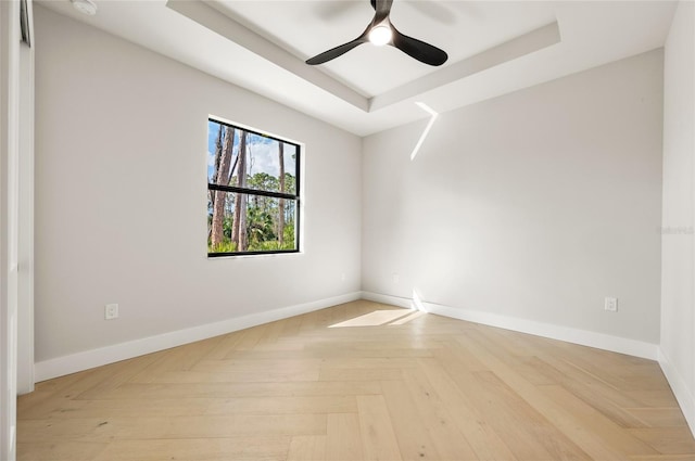 spare room with ceiling fan, light parquet flooring, and a tray ceiling